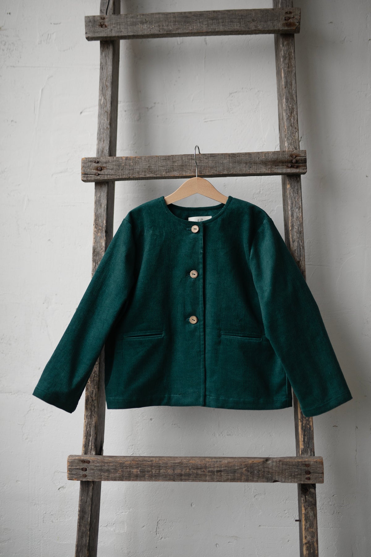A dark green jacket is hanging on a wooden ladder against a white wall.