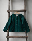 A dark green jacket is hanging on a wooden ladder against a white wall.