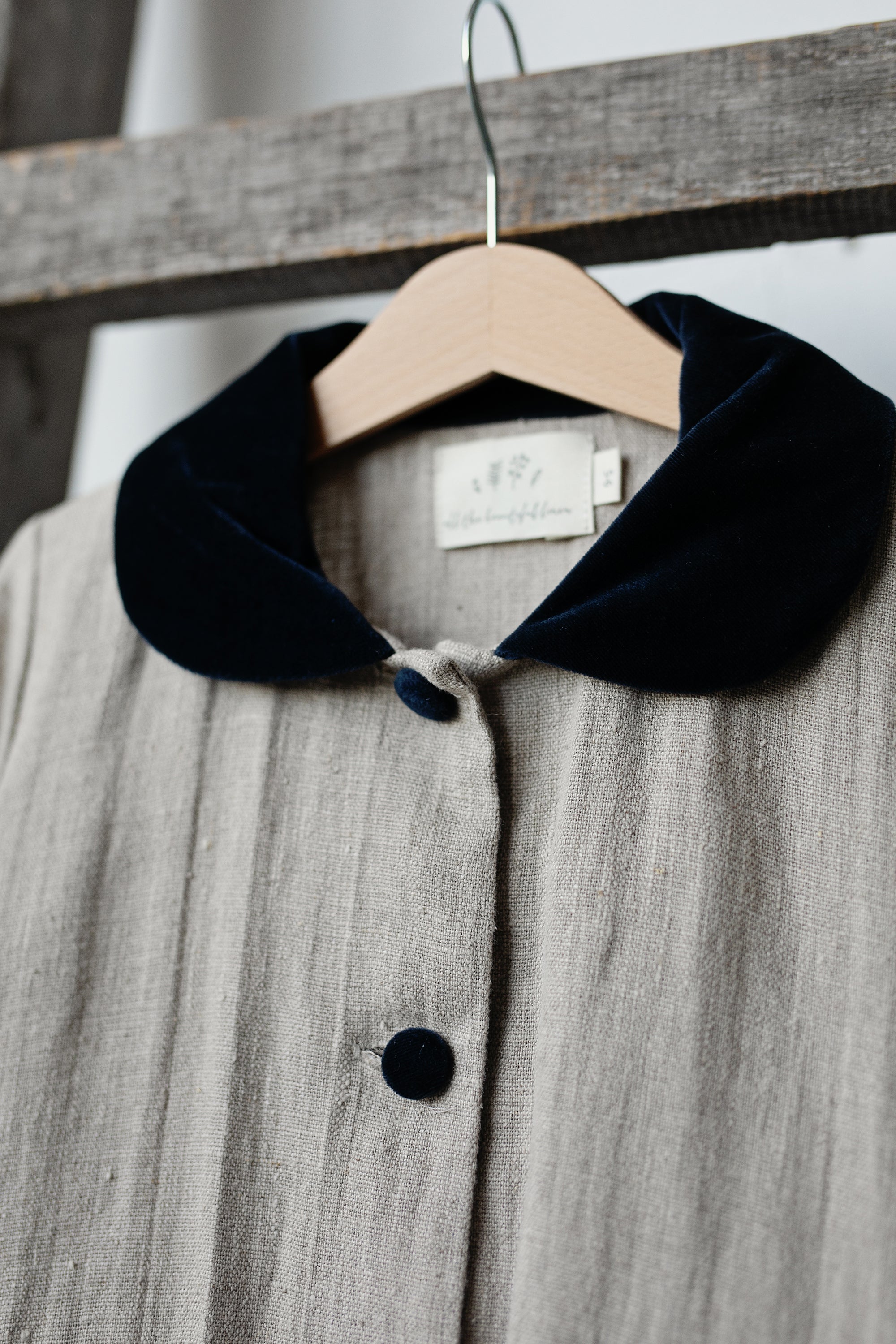A gray coat with a black collar and buttons is hanging on a wooden hanger.