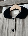A gray coat with a black collar and buttons is hanging on a wooden hanger.