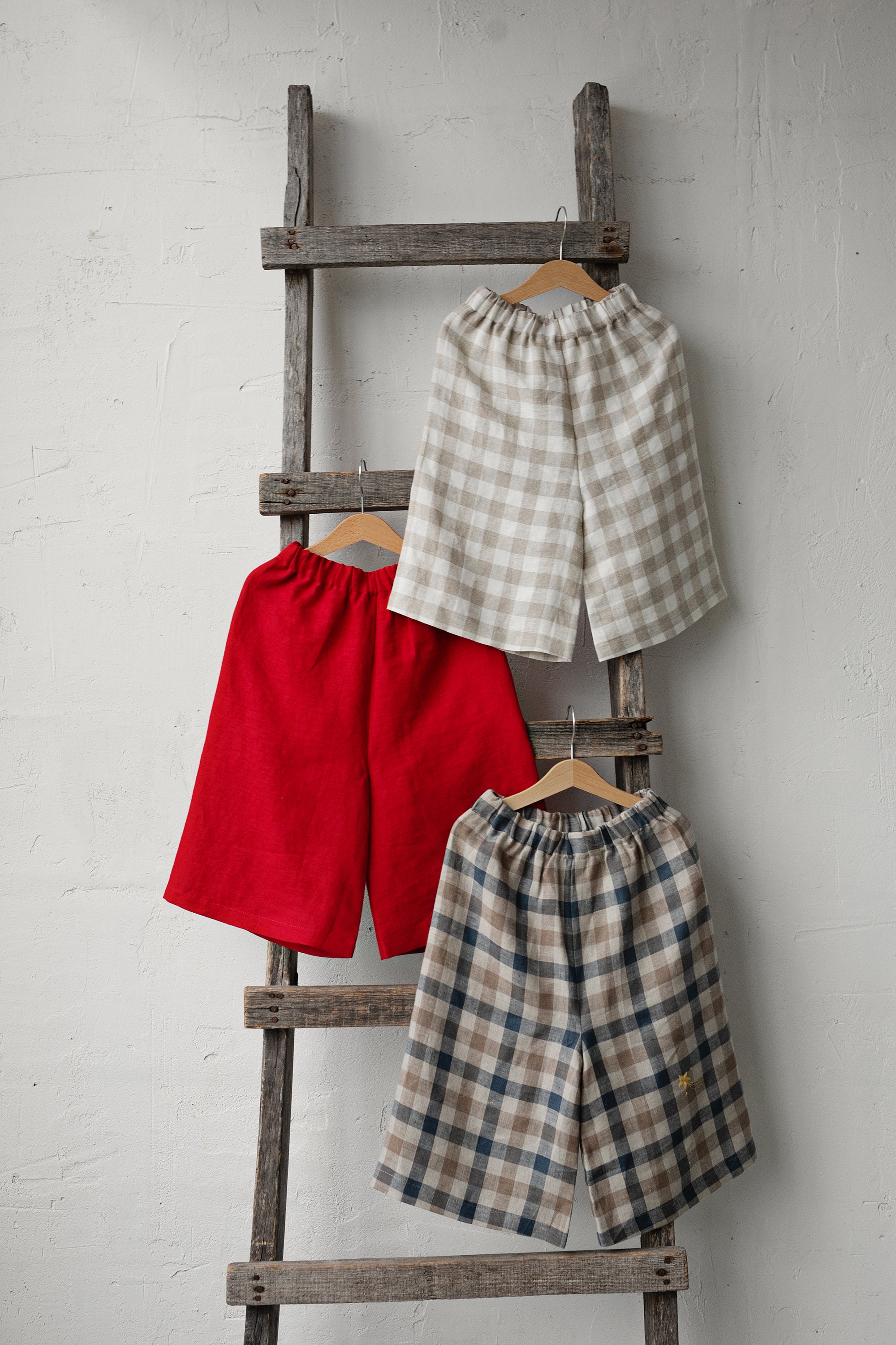 Three pairs of men's shorts hanging on a wooden ladder against a white wall.