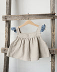A beige dress with blue accents hangs on a wooden ladder against a white wall.