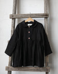 A black, button-up jacket is hanging on a wooden ladder against a white wall.