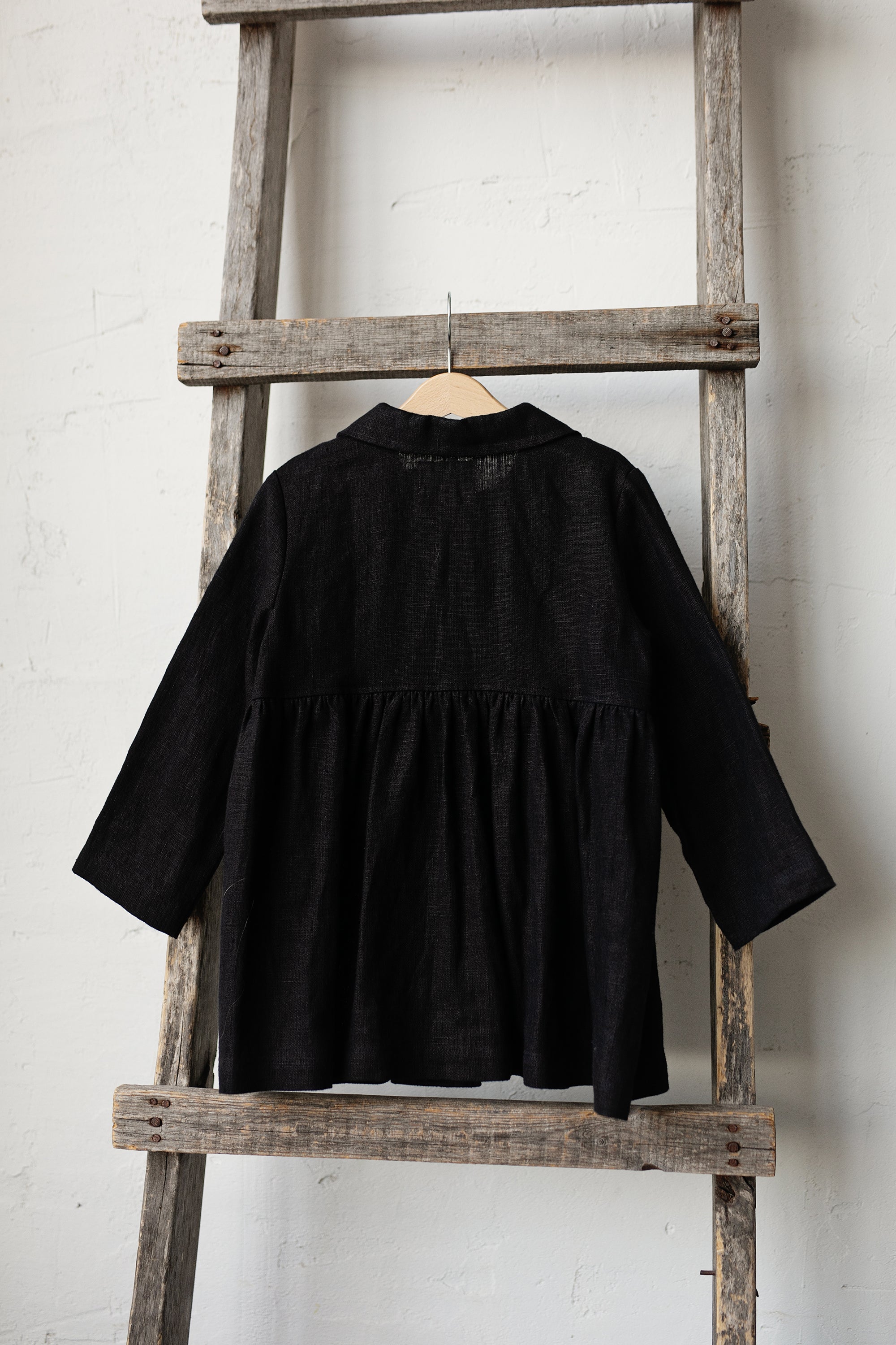 A black jacket is hanging on a wooden ladder against a white wall.