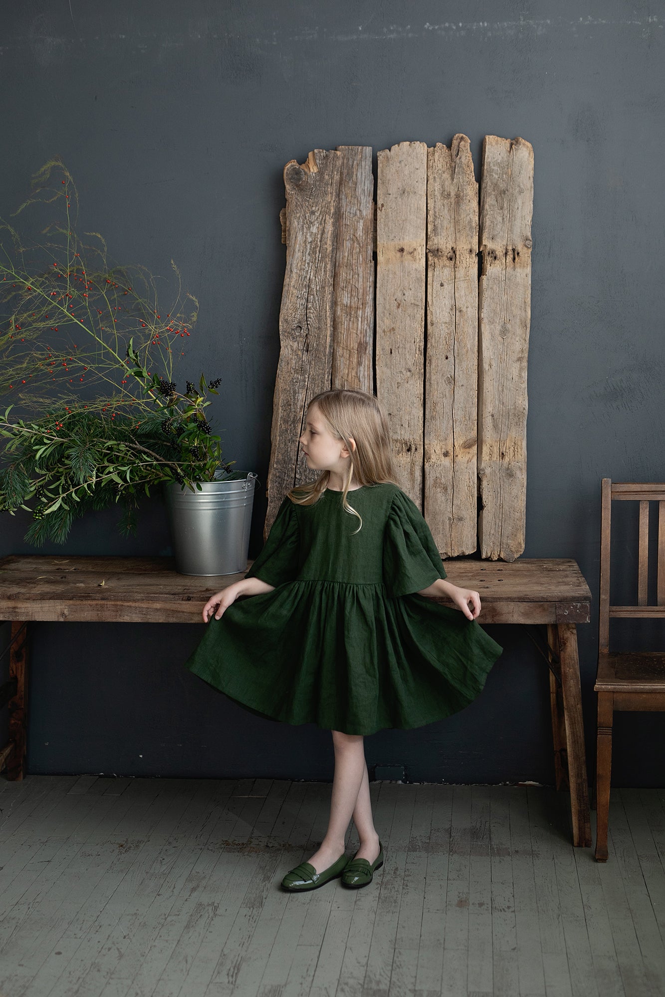 a little girl in a green dress standing in front of a wooden bench