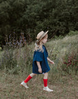 a little girl in a blue dress and hat walking through a field