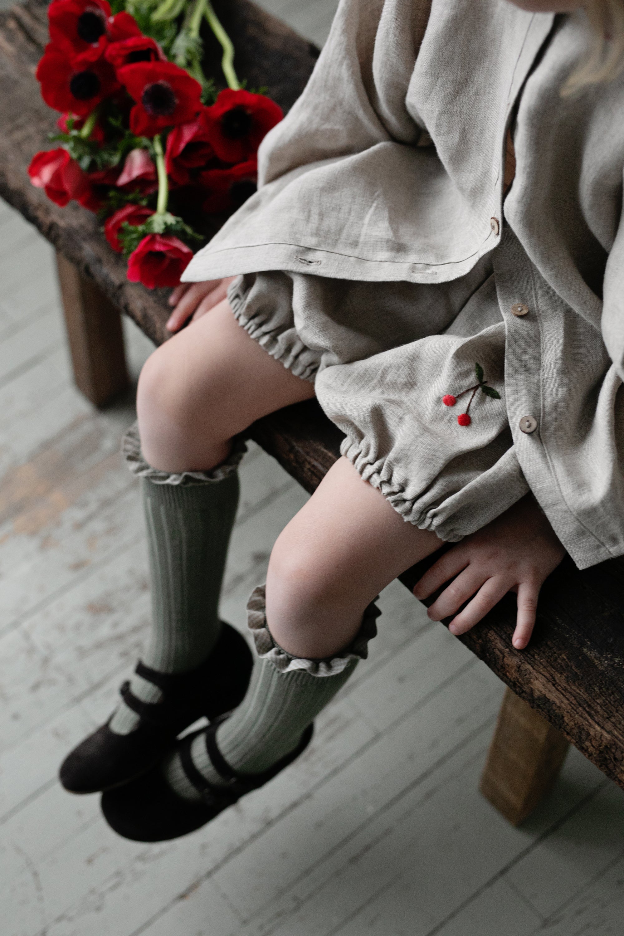 a little girl sitting on a bench next to a bunch of flowers